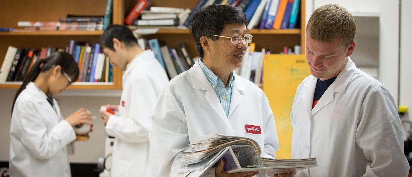Four people in white lab coats in front of a shelf of books.